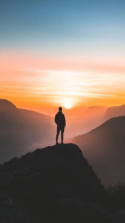 Person on cliff overlooking sunset landscape